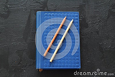 Hardcover beige book and pencils on black slate board. Stock Photo
