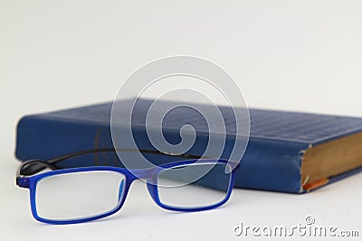 Hardcover beige book and reading glasses on white slate board. Stock Photo