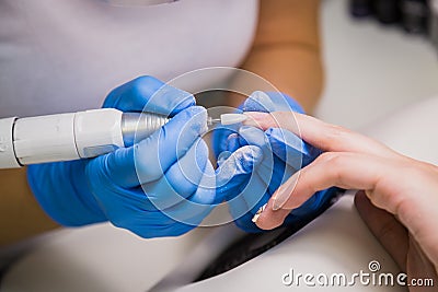 Hardware manicure in a salon. Manicurist is applying electric nail file drill Stock Photo