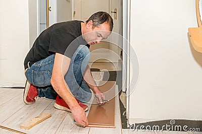 Hardworking man with a physical handicap in his hand that has several amputated fingers working on laying the floor of his house. Stock Photo