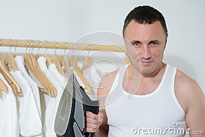 Hardworking man taking care of clothes doing household chores, posing against wooden clothes hanger Housework and Stock Photo