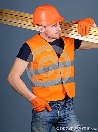 Hardy labourer concept. Carpenter, woodworker, labourer, builder on busy face carries wooden beams on shoulder. Man in Stock Photo