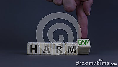 From harm to harmony. Businessman turns the wooden cube and changes word harm to harmony. Beautiful grey table, grey background. Stock Photo