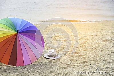 Hat, sunglasses and rainbow colored umbrella on a tropical beach Stock Photo