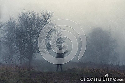 A haunted figure on a path on a hill on a moody, foggy winters day. With an abstract, grain, grunge edit Stock Photo