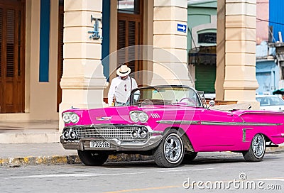 Cuban man on his american pink 1958 Chevrolet classic car convertible in the old town from Editorial Stock Photo