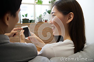 Young Asian couple sitting on sofa are looking at the cellphone. Stock Photo