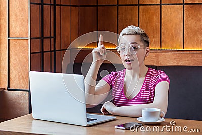 Have idea! Portrait of creative positive attractive young girl freelancer in pink t-shirt is sitting in cafe and working on laptop Stock Photo