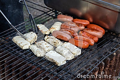 Having a barbeque with hot coals outside, turing halloumi cheese with tongs on a barbecue or bbq Stock Photo