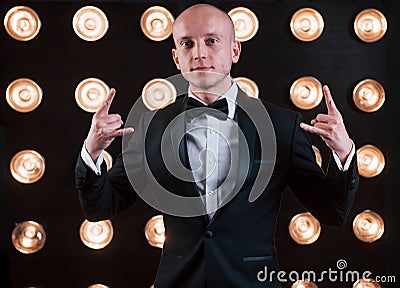 Having fun at his free time. Magician in black suit standing in the room with special lighting at backstage Stock Photo