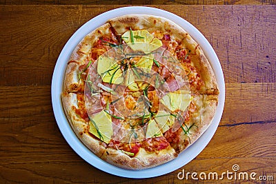 Hawaiian Pizza. A Ham and Pineapple Pizza on a white plate on a wooden table for lunch. Pizza is enjoyed world wide by hungry Stock Photo