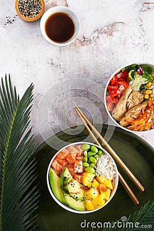 Hawaiian trendy poke bowls with salmon, heura soy protein or vegan chicken, variety vegetables, mango served in bowl on tropical Stock Photo