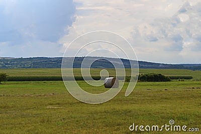 Hay bale on the meadow with blue sky and hills Stock Photo