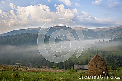 Hay stack on a green meadow in the mountains in the morning Stock Photo
