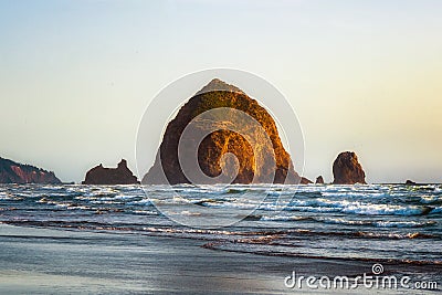 The Haystack Rock sea stack at high tide at sunset. Natural iconic landmark located in Cannon Beach, Oregon Coast Stock Photo