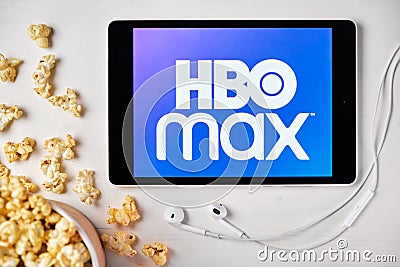 HBO MAX logo on the screen of the tablet laying on the white table and sprinkled popcorn on it. Apple earphones near the Editorial Stock Photo