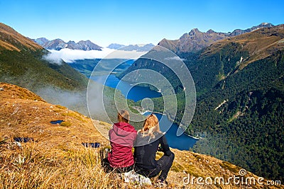 Back view of couple travellers in front of stunning mountain valley lake view, Key Summit Route Burn Track, Fiordland, New Zealand Stock Photo