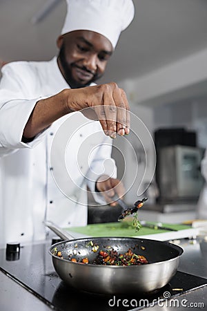 Head cook throwing fresh chopped herbs in pan to improve taste of meal while in professional kitchen. Stock Photo