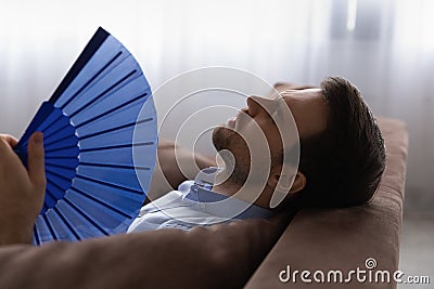 Head shot exhausted man waving paper fan, suffering from overheating Stock Photo