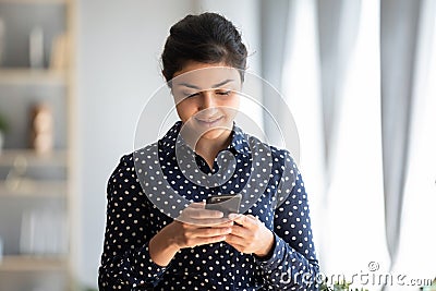 Pleasant millennial indian girl holding smartphone, reading good news sms. Stock Photo