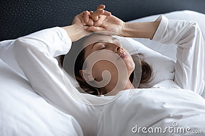 Stressed young brunette woman lying in bed with hands on head Stock Photo