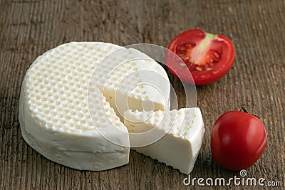 Head and slice of feta cheese on a wooden background with tomatoes. Stock Photo