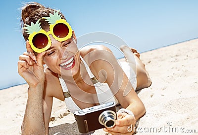 Woman in pineapple glasses checking photo at sandy beach Stock Photo
