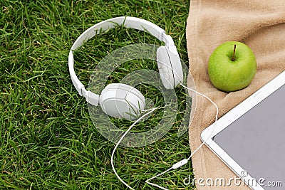 Headphones, electronic tablet and green apple for picnic in park Stock Photo