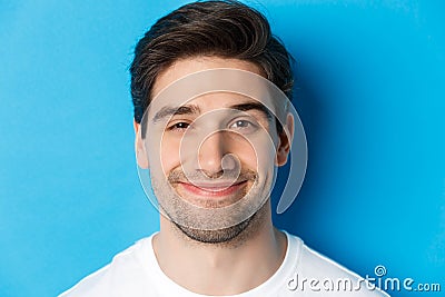 Headshot of attractive man smiling pleased, looking intrigued, standing over blue background Stock Photo