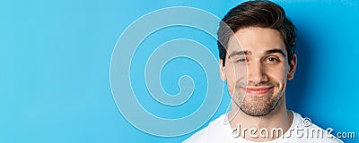 Headshot of attractive man smiling pleased, looking intrigued, standing over blue background Stock Photo