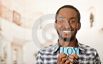 Headshot handsome man holding up small letters spelling the word joy and smiling to camera Stock Photo