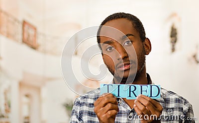 Headshot handsome man holding up small letters spelling the word tired and looking to camera Stock Photo
