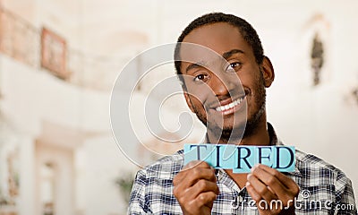 Headshot handsome man holding up small letters spelling the word tired and smiling to camera Stock Photo