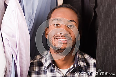 Headshot handsome young man standing inside wardrobe with clothes sorrounding, smiling to camera Stock Photo