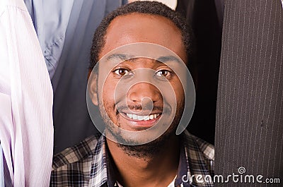 Headshot handsome young man standing inside wardrobe with clothes sorrounding, smiling to camera Stock Photo