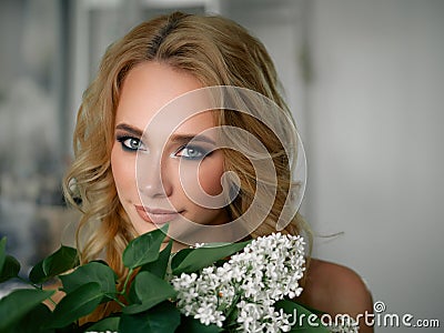 Headshot of happy beautiful blonde woman with lilac flower bouquet gorgeous trendy makeup beauty shiny skin posing indoors with Stock Photo