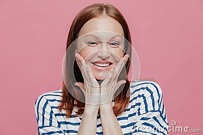 Headshot of smiling young European woman has make up, smiles broadly, keeps hands on cheeks, shows her beauty, expresses good Stock Photo