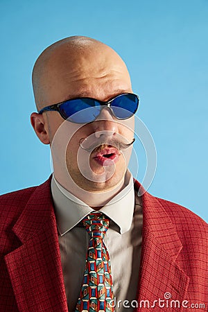 Headshot of whistles balded man with mustache dressed in business retro suit sneaking over blue studio background. Stock Photo