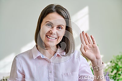 Headshot young smiling woman looking at camera greeting waving hand in home interior Stock Photo