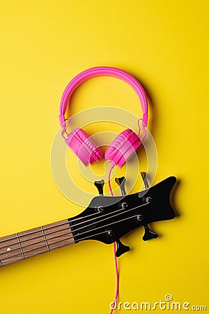 headstock of a five string guitar next to a pair of pink headsets Stock Photo