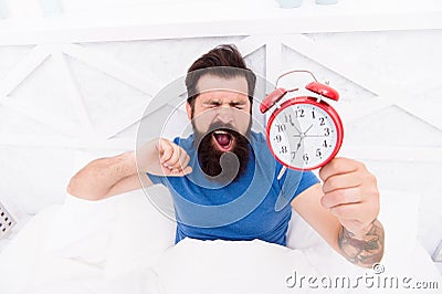 Health benefits of rising early. Waking up early gives more time. Hipster bearded man in bed with alarm clock. Time to Stock Photo