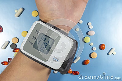 Health care. Closeup of wrist blood pressure monitor with colorful pills on blue background for medical design. Stock Photo