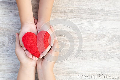 Adult and child hands holding handmade red heart on wooden background. Stock Photo