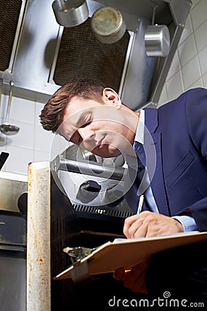 Health Inspector Looking At Oven In Commercial Kitchen Stock Photo