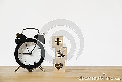 Health and medical icon on wood block and black analog alarm clock on wood desk for health insurance, nonstop medical service Stock Photo