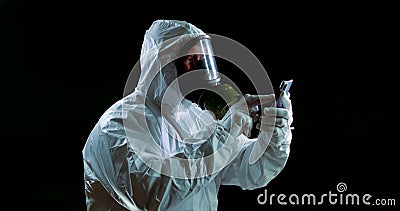 Health professional dressed coveralls and full face mask is sending urgent message by smartphone Stock Photo