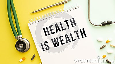 HEALTH IS WEALTH is written in a notebook on a color table next to pills and a stethoscope Stock Photo