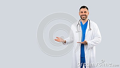 Healthcare ad. Positive male physician pointing aside at free space with two hands, panorama with free place for design Stock Photo