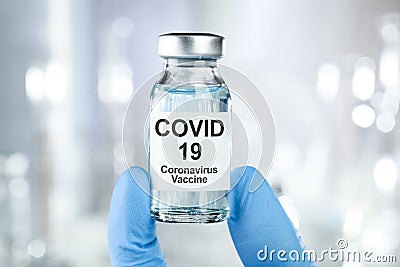 Healthcare cure concept with a hand in blue medical gloves holding Coronavirus, Covid 19 virus, vaccine vial Stock Photo