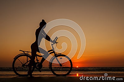 Healthy alone woman ride on bicycle on empty sunset Goa India beach Stock Photo